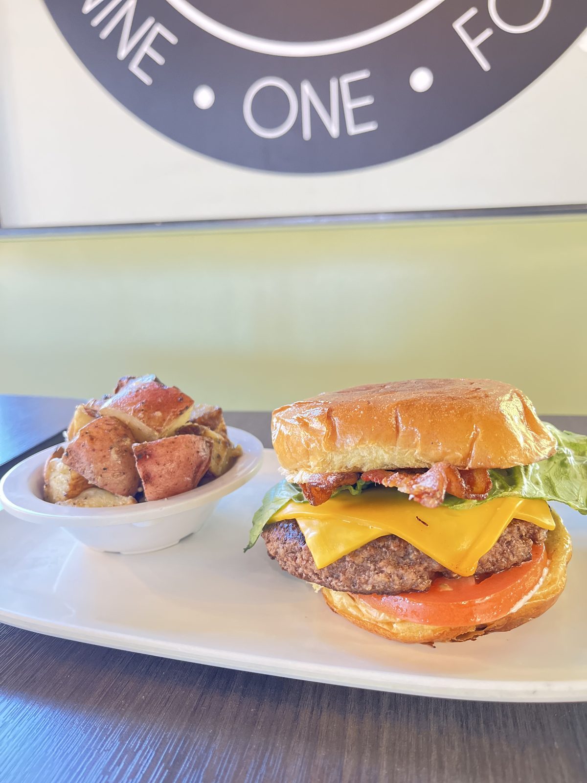 A bacon cheeseburger with roasted potatoes in front of the Nine One Four sign